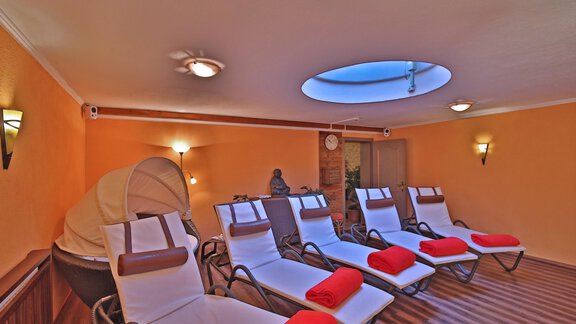 A relaxing room with loungers, red towels, and soft light. Above, there is a window that lets in daylight. - Pension "Zur alten Mühle" - Sölden