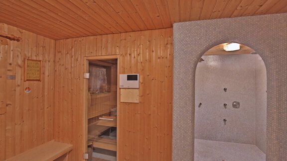 A cozy sauna with wooden paneling and benches. In the background, there is a shower area with tiled walls. - Pension "Zur alten Mühle" - Sölden