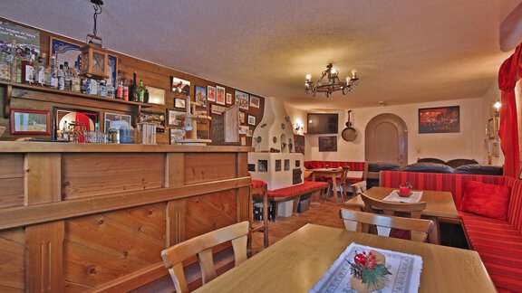 A cozy restaurant with wooden paneling and red benches. Pictures hang on the walls, and there is a well-equipped bar. - Pension "Zur alten Mühle" - Sölden