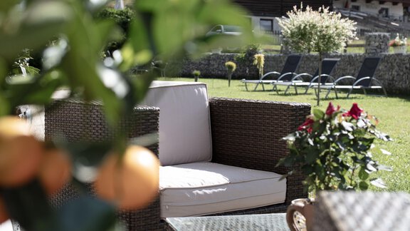 Ein gemütlicher Außenbereich mit einem Rattansofa und Blumen. Im Hintergrund sind Liegen und eine gepflegte Rasenfläche zu sehen. - Rustica Alpine B&B - Sölden