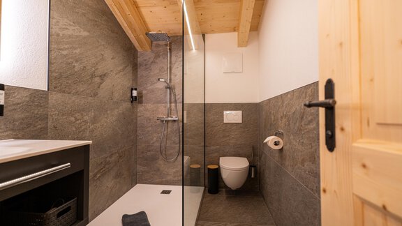 Ein modernes Badezimmer mit einer Glasdusche und Holzdetails. Die Wände sind in neutralen Grautönen gehalten und es gibt eine praktische Ablagefläche. - Selda Chalet - Sölden