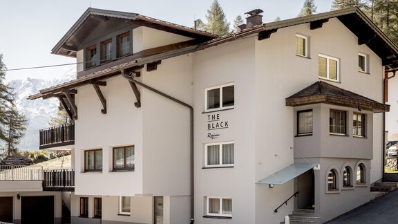 Ein modernes Gebäude mit mehreren Fenstern und einem einladenden Eingang. Das Haus hat einen alpinen Stil und ist von Bäumen umgeben. - THE BLACK by Regina - Sölden