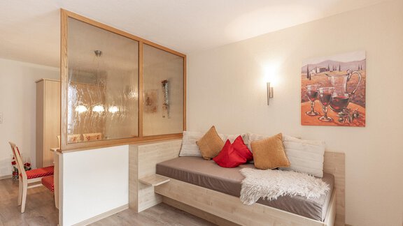 A cozy living space with a single bed - which is also suitable as a seating couch - and colorful cushions. - Trofana Appartements - Sölden