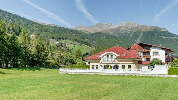 Ein schönes Haus mit rotem Dach in einer grünen Wiese. Im Hintergrund sind hohe Berge und ein klarer Himmel zu sehen. - Villa Castelbell - Sölden