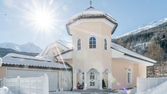 Ein wunderschönes Haus mit einer runden Türmchen und einer hellen Fassade im Schnee. Der sonnige Himmel und die Berge im Hintergrund schaffen eine malerische Winterlandschaft. - Villa Castelbell - Sölden