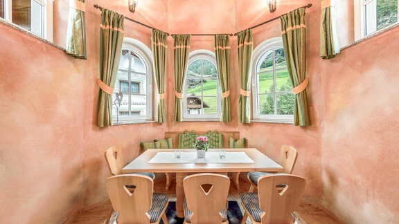 Ein gemütlicher Essbereich mit einem großen Tisch und Holzstühlen. Die Wände sind in warmen Farben gehalten und große Fenster bieten Blick ins Grüne. - Villa Castelbell - Sölden