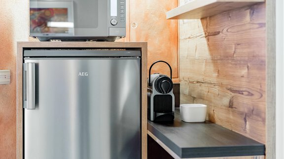 Eine moderne Küchenzeile mit einem Kühlschrank, einer Mikrowelle und einer Nespresso-Maschine. Die Wände sind in warmen Farben gehalten, und eine Holzregal ist sichtbar. - Villa Castelbell - Sölden