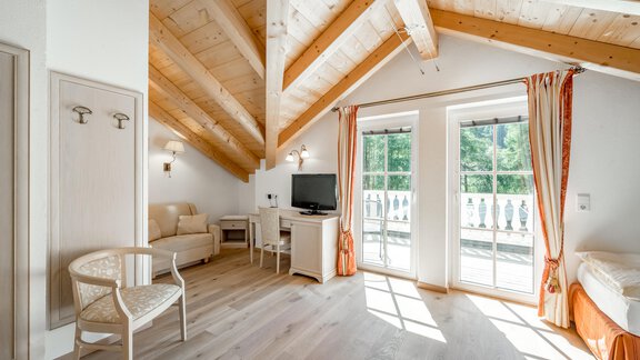 Ein helles Zimmer mit Holzdecke und großen Fenstern. Es gibt einen Fernseher, einen Tisch und Stühle sowie einen Balkon. - Villa Castelbell - Sölden