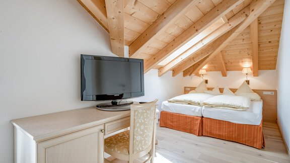 Ein gemütliches Zimmer im Dachgeschoss mit Holzdecken und einem großen Bett. Ein Schreibtisch und ein Fernseher befinden sich ebenfalls im Raum. - Villa Castelbell - Sölden