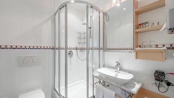Ein modernes Badezimmer mit einer Duschkabine und einem Waschbecken. Die Wände sind hell und es gibt praktische Ablagen für Toilettenartikel. - Villa Castelbell - Sölden