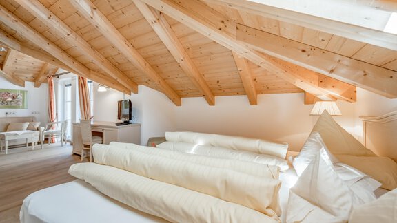 Ein gemütliches Dachzimmer mit Holzdecke und viel Tageslicht. Bettdecken und Kissen liegen ordentlich auf dem Bett. - Villa Castelbell - Sölden