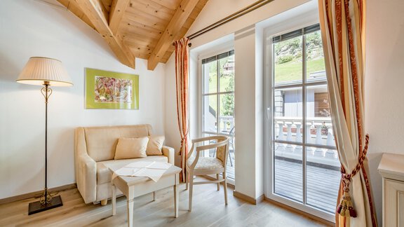 Ein gemütliches Wohnzimmer mit Holzdecke und großen Fenstern. Ein Sofa und ein Stuhl laden zum Entspannen ein. - Villa Castelbell - Sölden