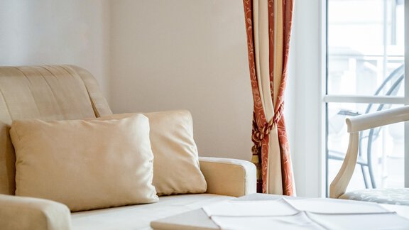 Ein helles Wohnzimmer mit einem beigen Sofa und einem kleinen Tisch. Vor den Fenstern hängen schöne Vorhänge. - Villa Castelbell - Sölden