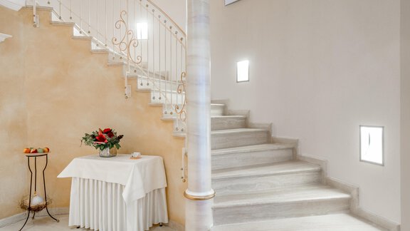 Eine elegante Treppe mit geschwungem Geländer führt nach oben. Neben der Treppe steht ein Tisch mit Blumenarrangement. - Villa Castelbell - Sölden