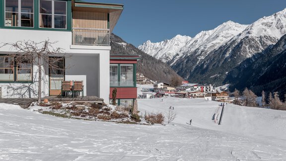 Ein modernes Gebäude in einer verschneiten Landschaft. Im Hintergrund sind majestätische Berge und ein kleines Dorf sichtbar. - zuckerhütl NATURAPPART - Sölden
