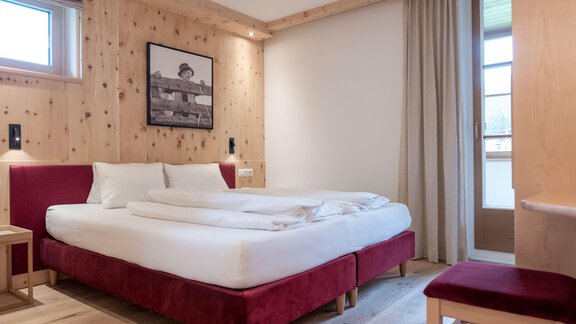 Ein modernes Schlafzimmer mit einem großen Doppelbett und rotem Bezug. Die Wände sind mit hellem Holz verkleidet und es gibt ein Fenster mit Vorhängen. - zuckerhütl NATURAPPART - Sölden