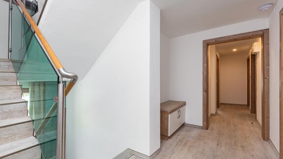 A bright hallway with a modern staircase and a small seating area. The walls are white and the floor is made of wood. - Garni Stefani - Vent