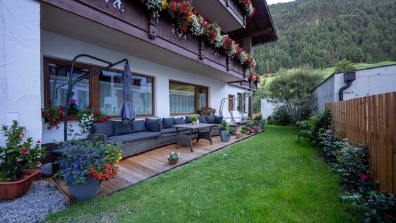 A beautifully decorated garden with a cozy seating area in front of a house. Colorful flowers and a well-kept lawn give the surroundings an inviting atmosphere. - Gästehaus Edelweiss - Vent