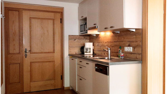 Eine moderne Küche mit hellen Schränken und einer Holzverkleidung. Die Ausstattung umfasst einen Herd, eine Spüle und eine Kaffeemaschine. - Gästehaus Soldanella - Vent