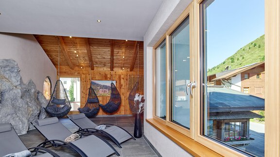Ein modernes Wellnessbereich mit Liegestühlen und großen Fenstern. Die Aussicht zeigt eine grüne Landschaft und eine Holzarchitektur. - Hotel Vent - Vent