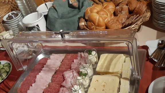 A breakfast buffet with various types of sausages and cheeses. In the background, fresh rolls and dishes can be seen. - Mein Weisskugel - Vent