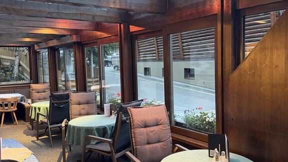 A cozy conservatory with wooden cladding and large windows. The tables are decorated with green tablecloths and provide space for guests. - Mein Weisskugel - Vent