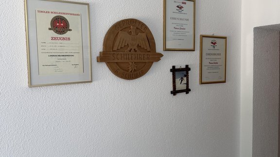 On a wall hang several certificates of honor and awards. In the center is a golden emblem. - Mein Weisskugel - Vent