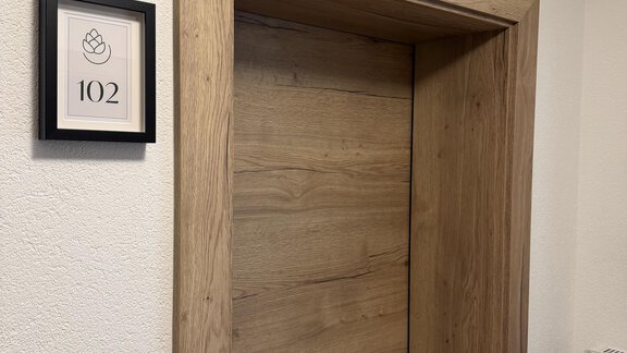 A wooden staircase with an open door. Next to the door is a sign with the number 102. - Mein Weisskugel - Vent