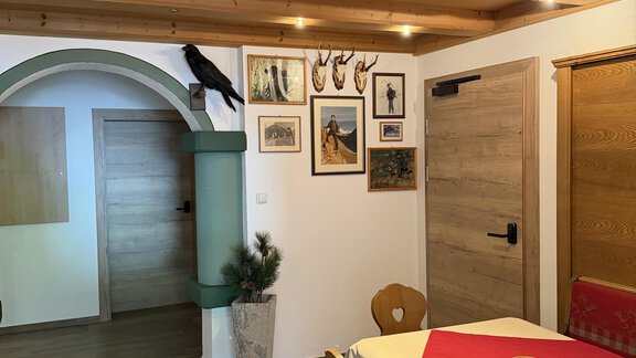A cozy room with a wooden beam ceiling and a table covered with a red tablecloth. Pictures and decorations hang on the walls, creating an inviting atmosphere. - Mein Weisskugel - Vent