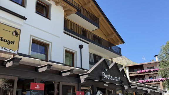 A cozy restaurant with a wooden veranda and blooming plants. The building features traditional alpine architecture and stands under a blue sky. - Mein Weisskugel - Vent