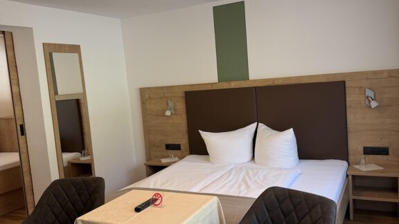 A cozy room with a double bed, a table, and two chairs. The decor is modern and minimalist. - Mein Weisskugel - Vent