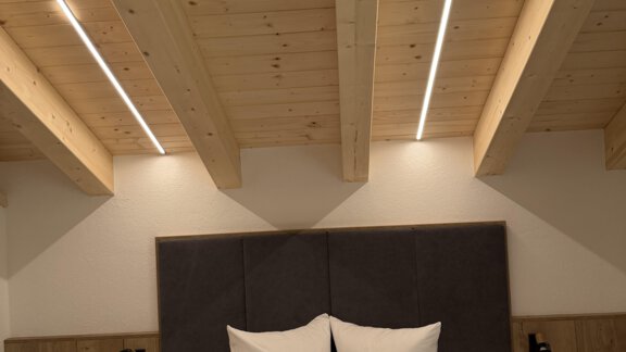 A modern bedroom with a wooden ceiling and soft lighting. The bed is adorned with white pillows and elegant bedding. - Mein Weisskugel - Vent