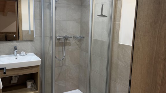 A modern bathroom with a glass shower and a sink. The walls are designed in neutral shades, and there is soft lighting. - Mein Weisskugel - Vent
