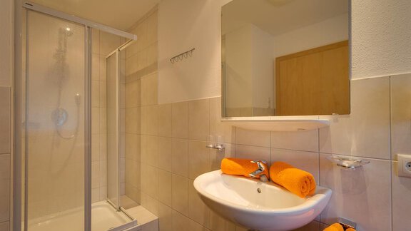 A modern bathroom with a shower and a sink. Towels in vibrant orange are neatly arranged. - Apart Praxmarer - Zwieselstein