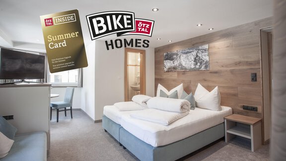 Ein modernes Hotelzimmer mit einem Doppelbett und einem gemütlichen Sitzbereich. Im Bild sind auch die Summer Card und das Logo von Bike Homes zu sehen. - Garni Ötztal ROOMS & APARTS - Zwieselstein