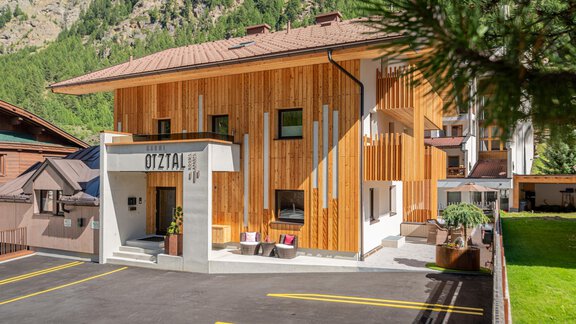 A modern building with wooden cladding in a mountainous environment. The entrance is clearly visible, and there is a parking lot in front of the house. - Garni Ötztal ROOMS & APARTS - Zwieselstein