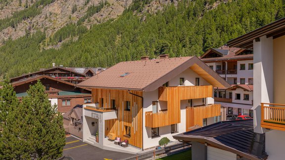 Ein modernes Gebäude mit Holzverkleidung in einer malerischen Berglandschaft. Umgeben von Bäumen und anderen chalets, bietet es eine ruhige Atmosphäre. - Garni Ötztal ROOMS & APARTS - Zwieselstein
