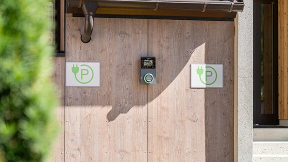 Eine Wand mit zwei Parksymbolen für Elektrofahrzeuge und einem Ladegerät. Die Oberfläche ist aus Holz und die Umgebung wirkt modern und einladend. - Garni Ötztal ROOMS & APARTS - Zwieselstein