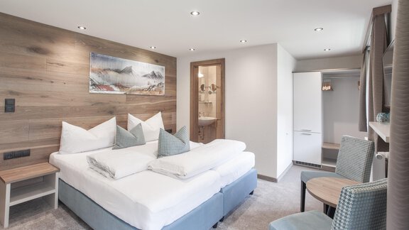 A modern bedroom with a large double bed and light wood design. There is a small seating area and a wardrobe. - Garni Ötztal ROOMS & APARTS - Zwieselstein