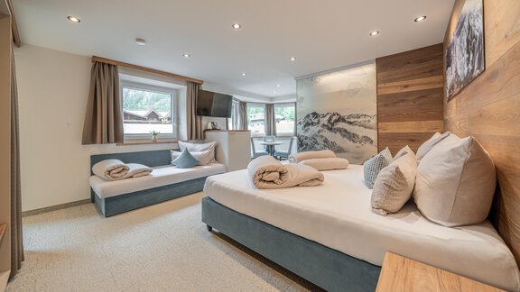 A modern bedroom with two beds and cozy pillows. The room has large windows and warm wood accents. - Garni Ötztal ROOMS & APARTS - Zwieselstein