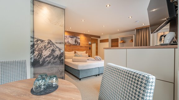 A modern hotel room with a large bed and a cozy seating area. The walls are stylishly decorated and there is a table with chairs. - Garni Ötztal ROOMS & APARTS - Zwieselstein