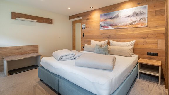 A modern bedroom with a large bed and cozy bedding. The walls are made of wood, and there is a nice picture above the bed. - Garni Ötztal ROOMS & APARTS - Zwieselstein