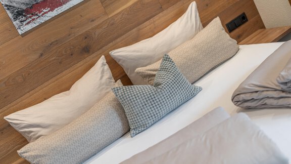 Ein gemütliches Schlafzimmer mit einem Bett und mehreren Kissen. Die Wände sind aus Holz und es gibt dekorative Elemente im Hintergrund. - Garni Ötztal ROOMS & APARTS - Zwieselstein