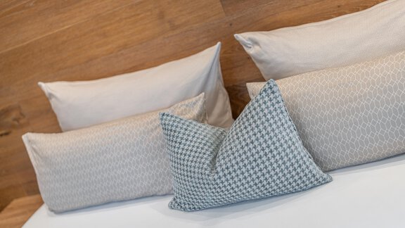 A cozy bed with several pillows. The pillows have different textures and patterns against a wooden wall. - Garni Ötztal ROOMS & APARTS - Zwieselstein