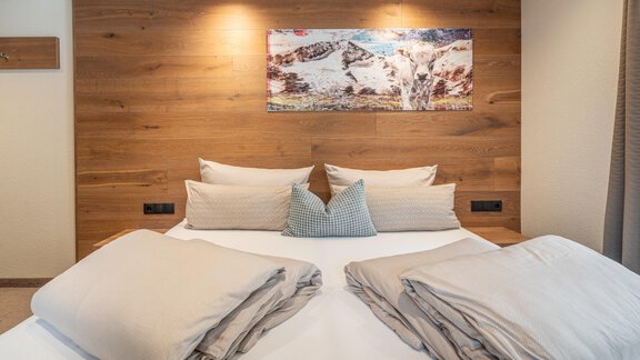 Ein gemütliches Schlafzimmer mit einem Doppelbett und dekorativen Kissen. An der Wand hängt ein Bild von einer Berglandschaft. - Garni Ötztal ROOMS & APARTS - Zwieselstein