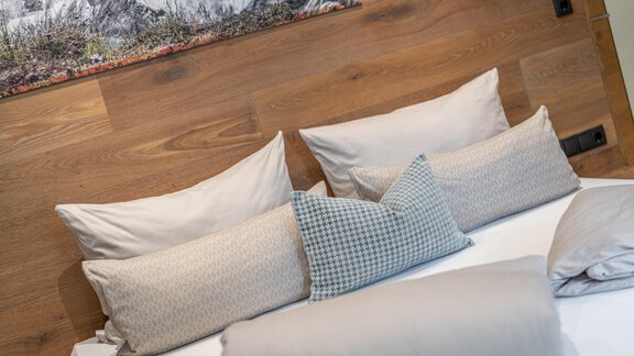 A cozy bed with many pillows and a wooden paneling in the background. The colors are neutral and create a relaxed atmosphere. - Garni Ötztal ROOMS & APARTS - Zwieselstein