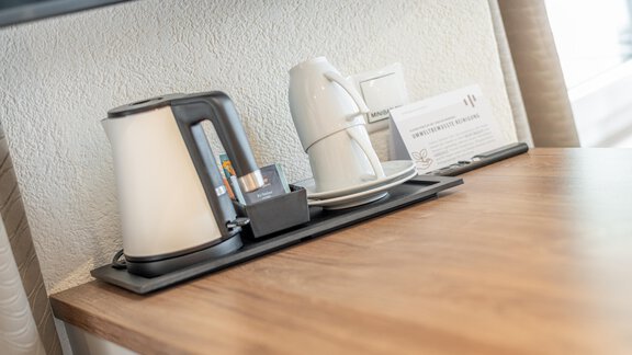 An elegant kettle is standing on a table, next to it are a cup and another vessel. The arrangement is tidy and modern. - Garni Ötztal ROOMS & APARTS - Zwieselstein