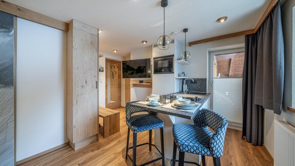 A modern kitchen with wooden and glass elements. The dining area is cozy, equipped with blue chairs. - Garni Ötztal ROOMS & APARTS - Zwieselstein