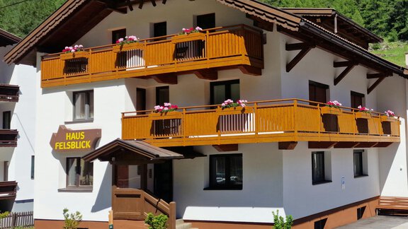 Ein modernes Haus mit Balkonen und blühenden Pflanzen. Die Fassade ist in Weiß und Braun gehalten, umgeben von grüner Natur. - Haus Felsblick - Zwieselstein