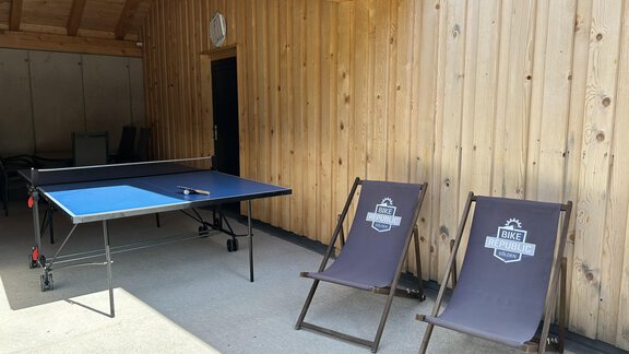 A cozy outdoor area with a ping pong table and two lounge chairs. The wall is made of wood, and the atmosphere is relaxing. - Hochstatt Appartements - Zwieselstein